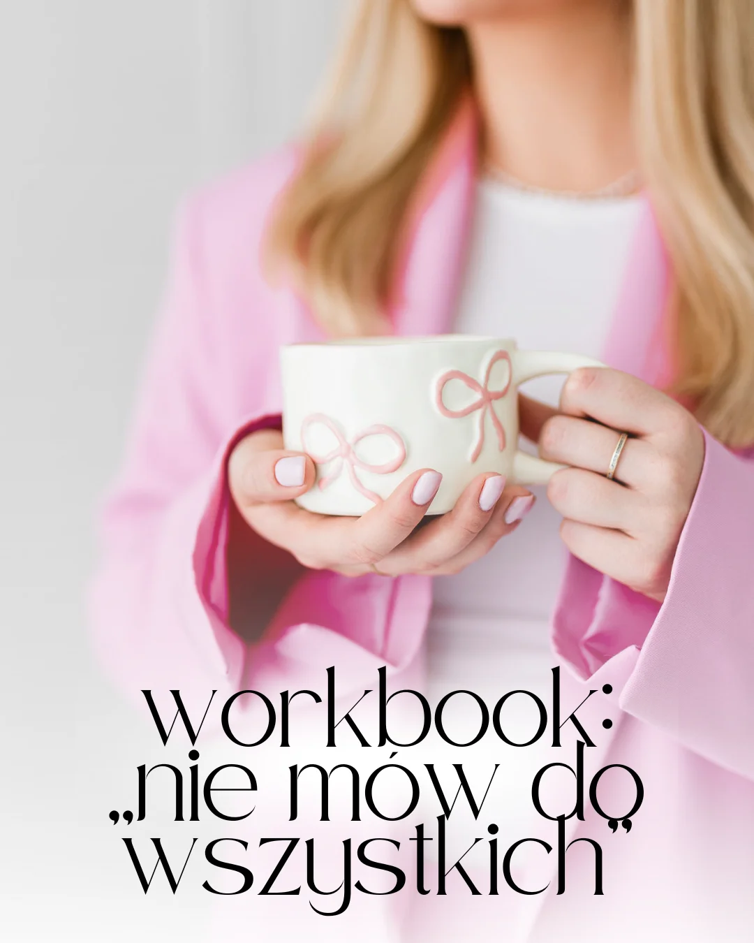 Młoda kobieta o blond włosach stoi z białą filiżanką. Ma na sobie różowy garnitur.