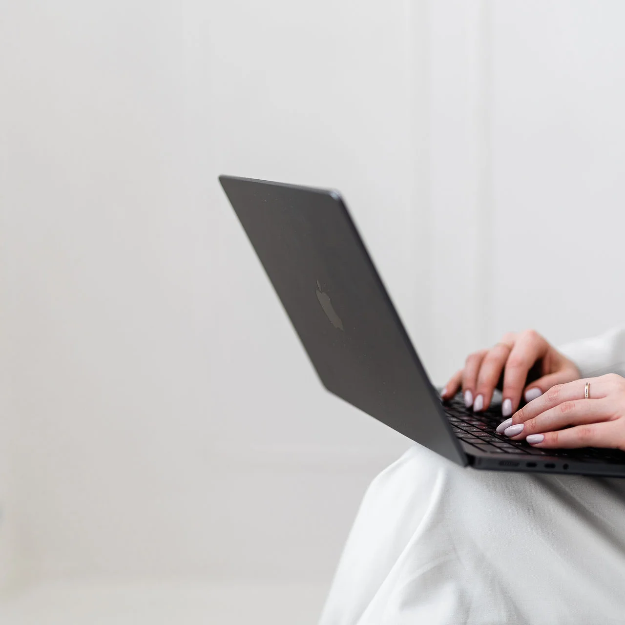 Ujęcie dłoni i czarnego laptopa na tle białej ściany.