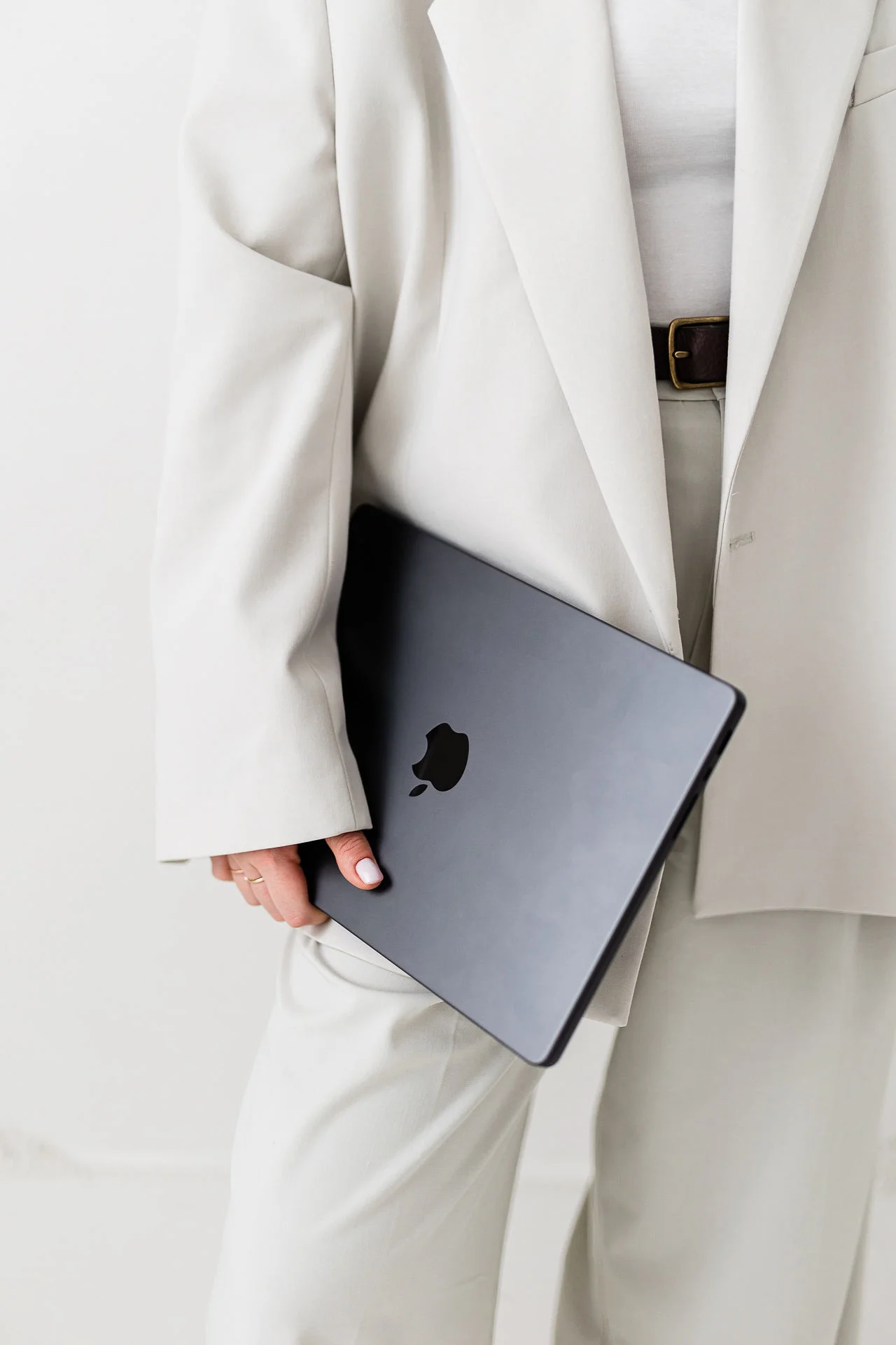 Kobieta w białym garniturze stoi i trzyma w dłoni szary laptop.